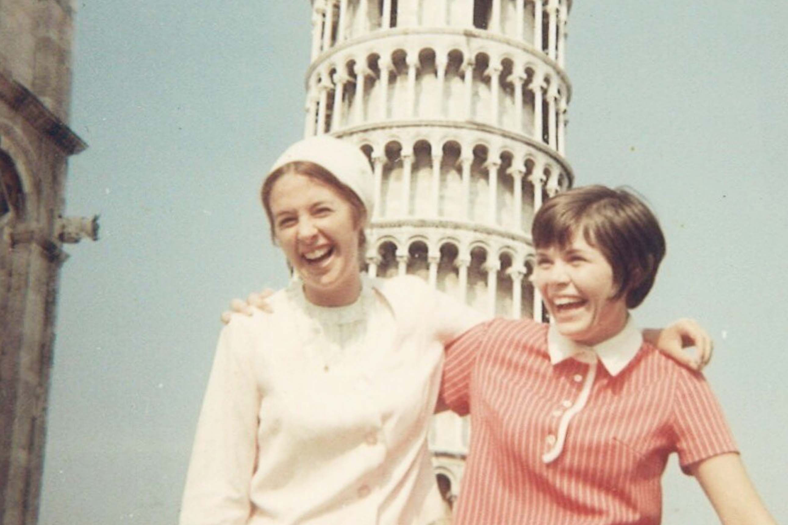 Two students in front of the Leaning Tower of Pisa laughing in a vintage photograph