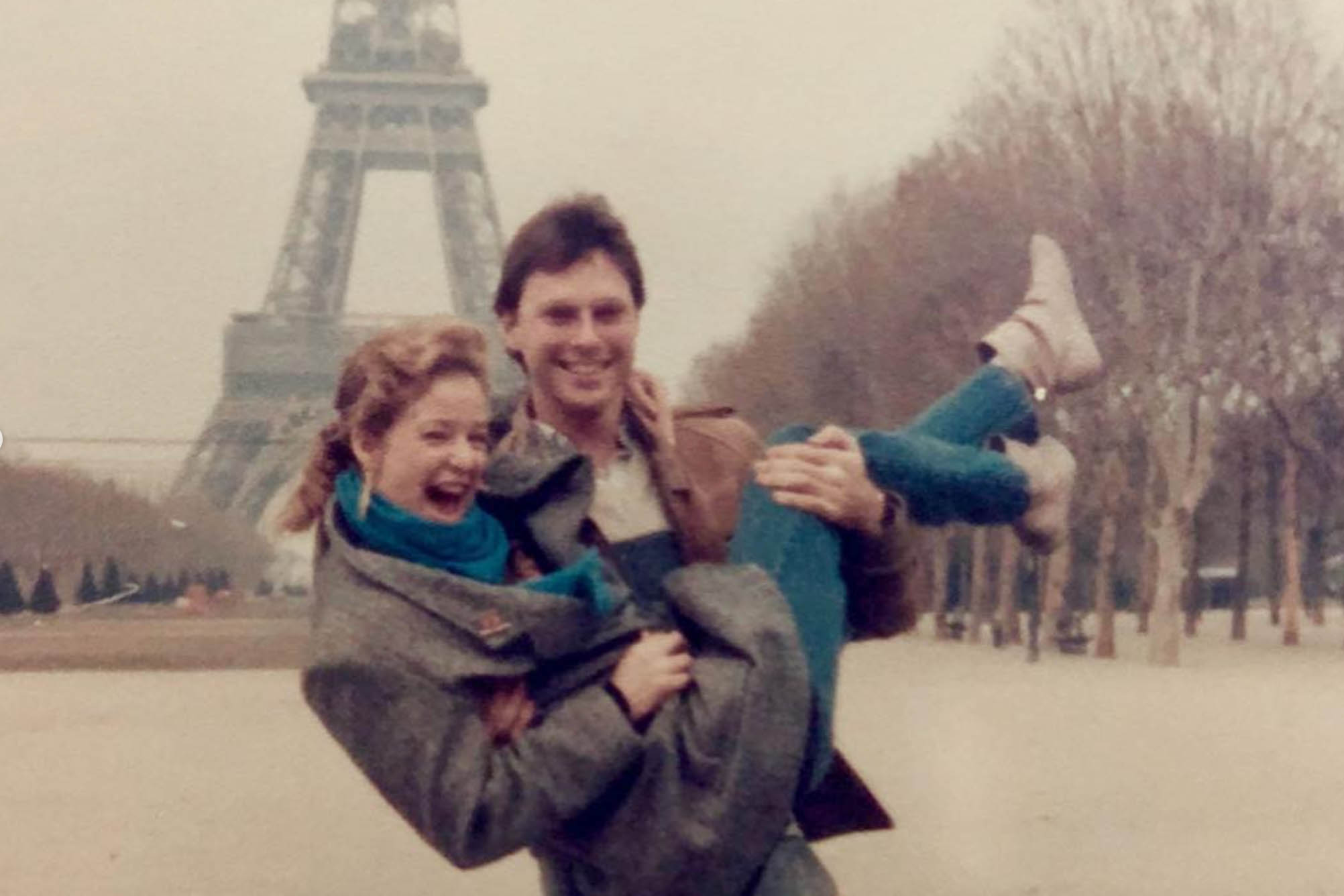 Two students in a vintage photo pose laughing in front of the Eiffel Tower