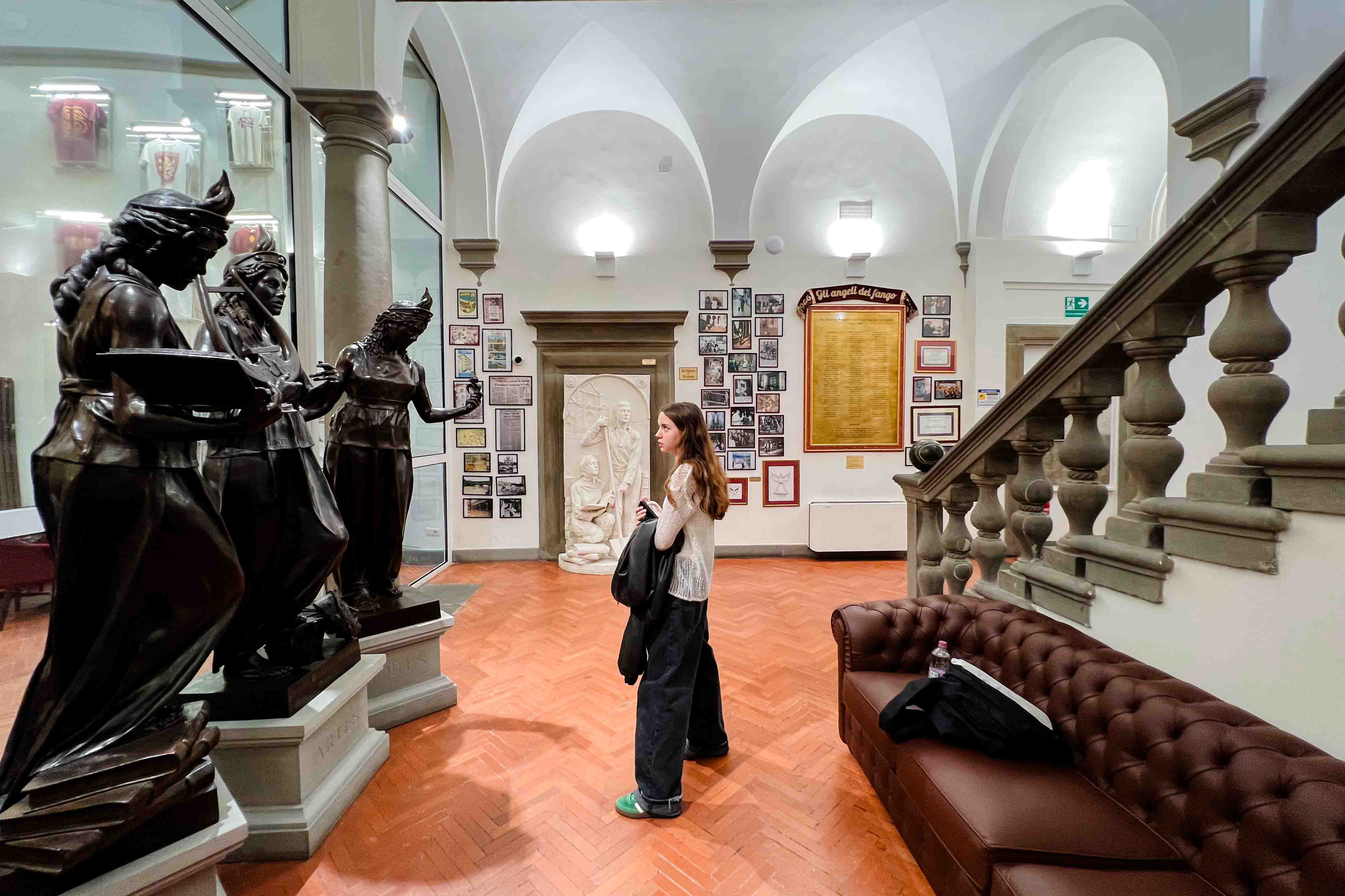 A student looks up at the 'Vires, Artes, Mores' statues that greet you when you walk into the lobby at FSU Florence.