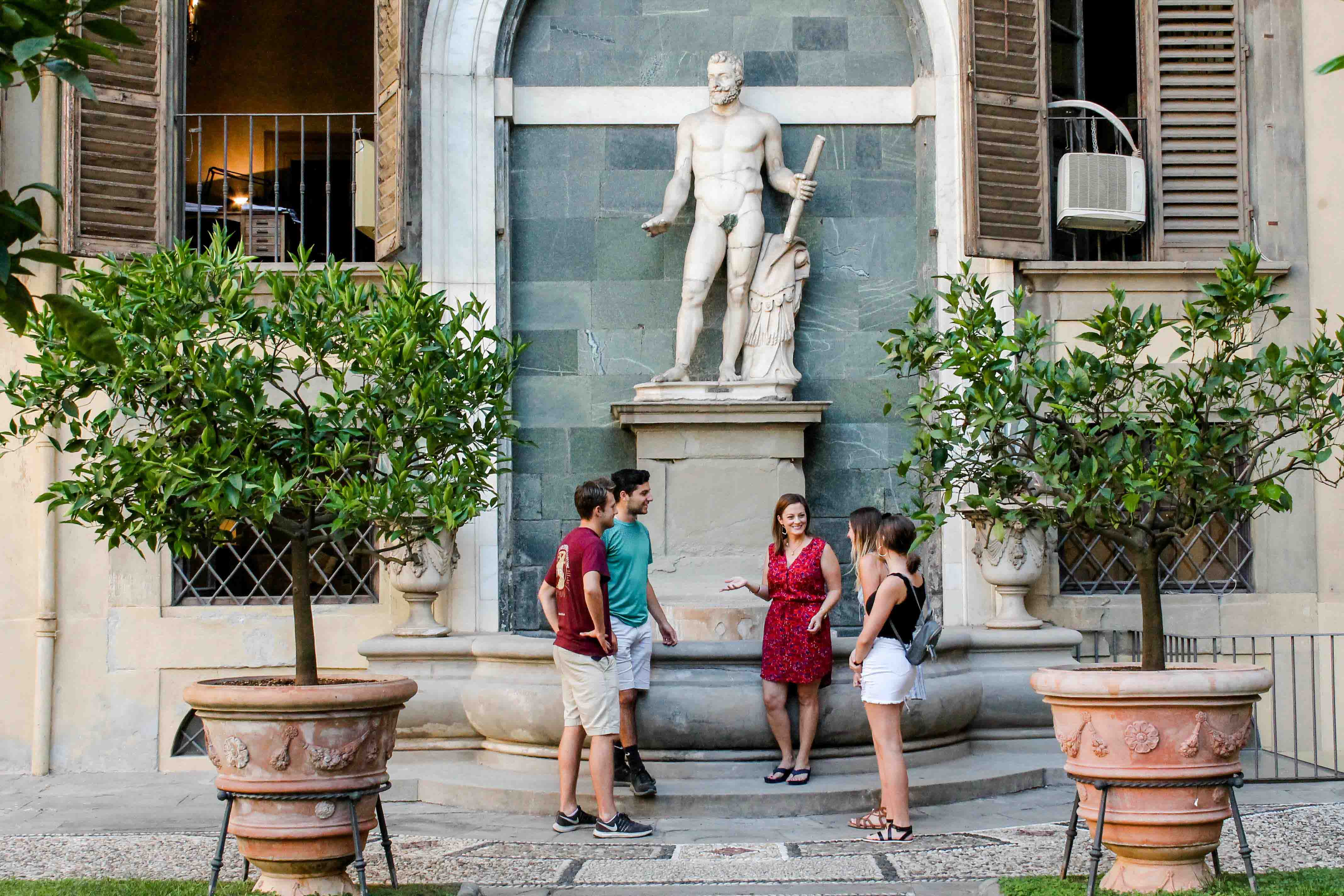 A faculty member lectures in front of a statue in the streets of Florence to her students.