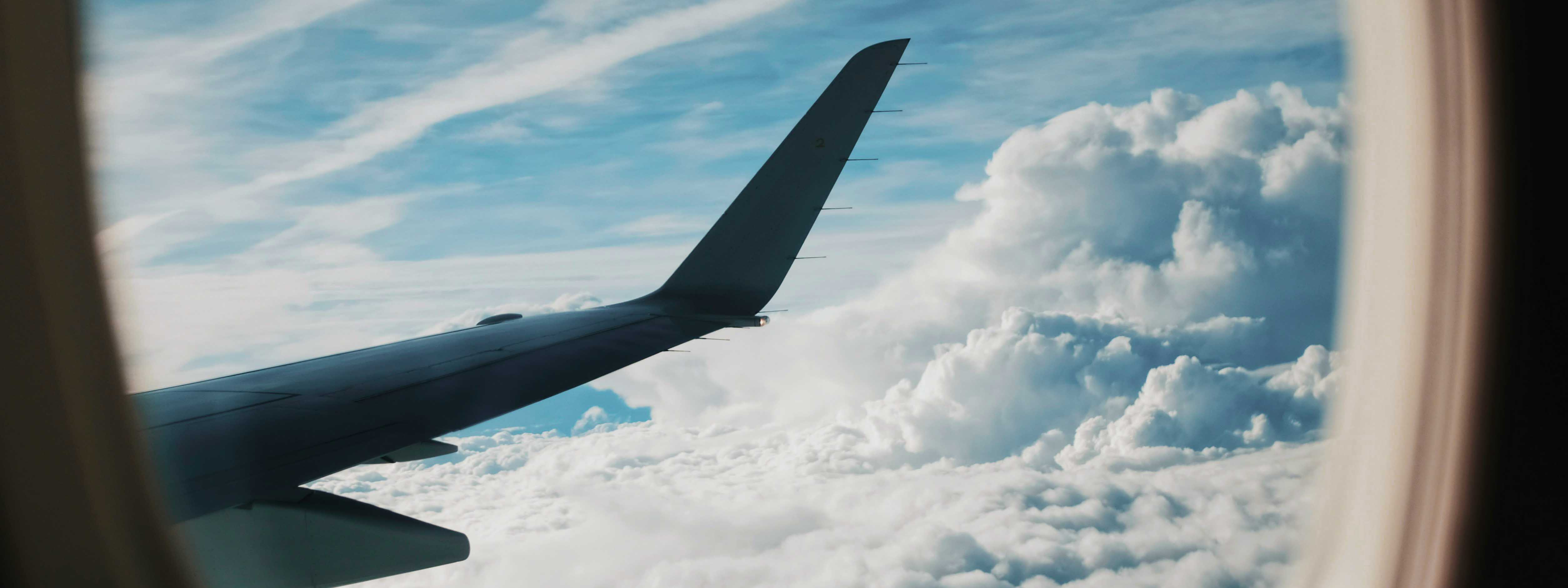 A view of an airplane wing out of an airplane window with clouds below.