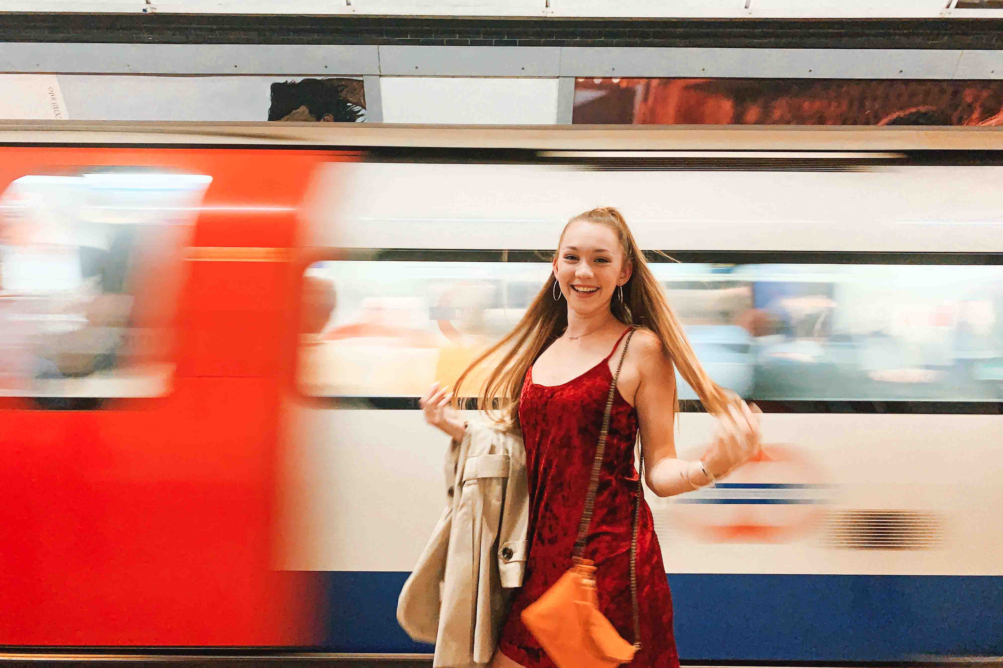 A student poses in front of a moving London train on the Underground platform