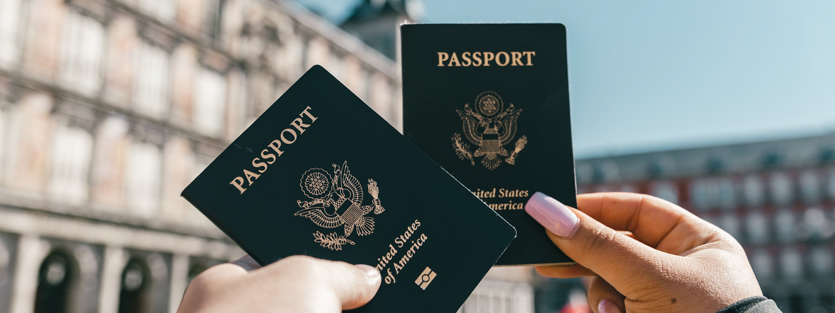 Hands holding up two US passports in an international city.