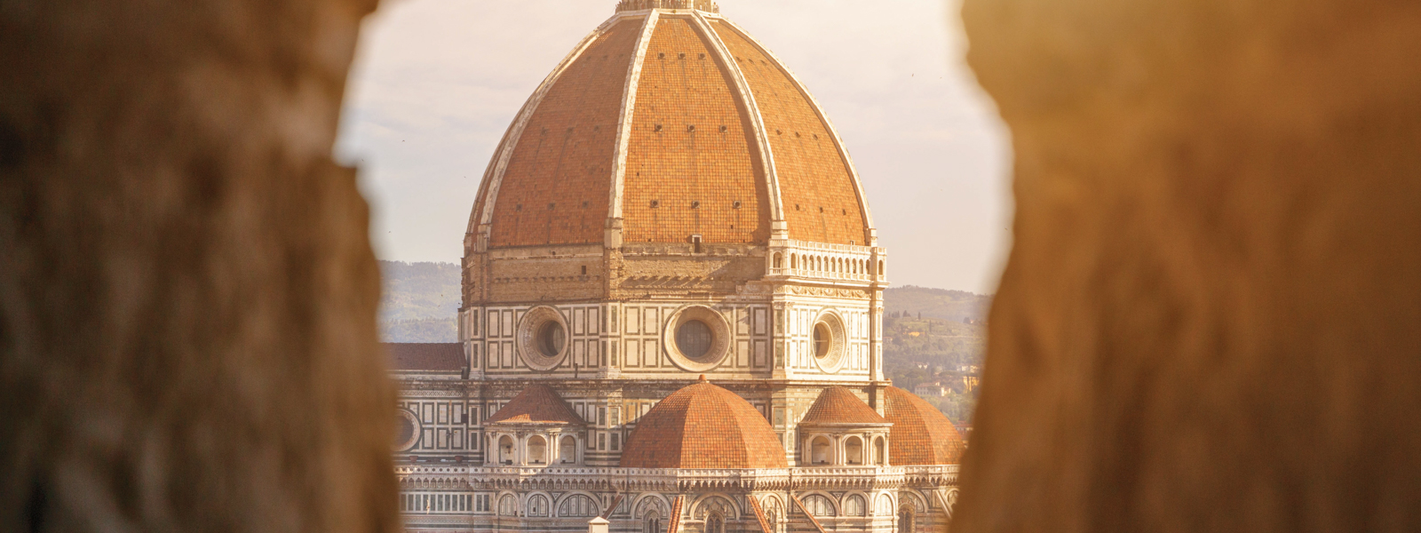 A view of the Duomo between two stone walls.
