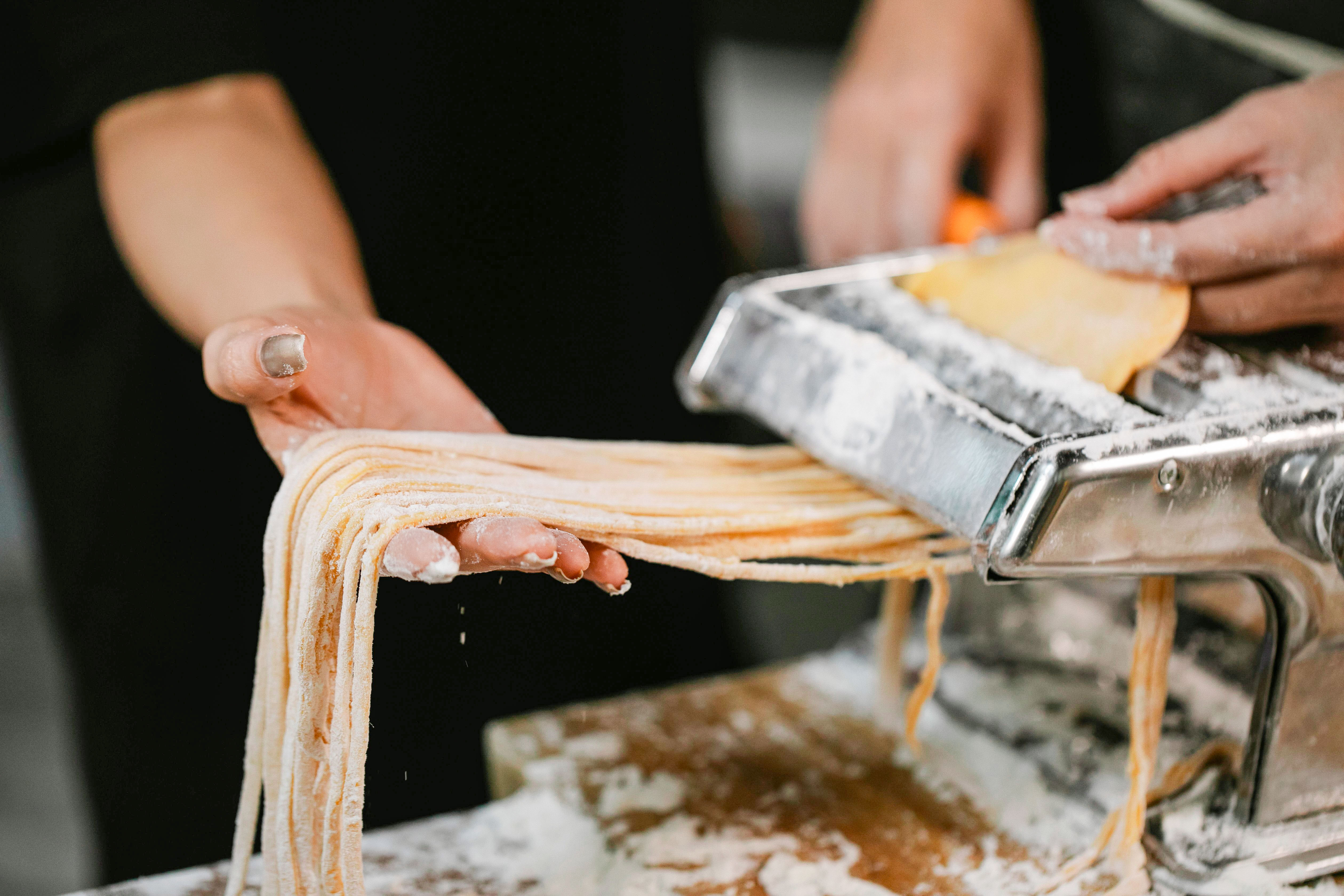 A photo of hands holding pasta as it is cut in a pasta making machine.