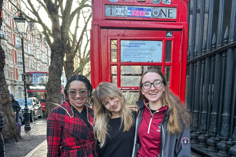 Students posing in front of an iconic red phone booth in London.