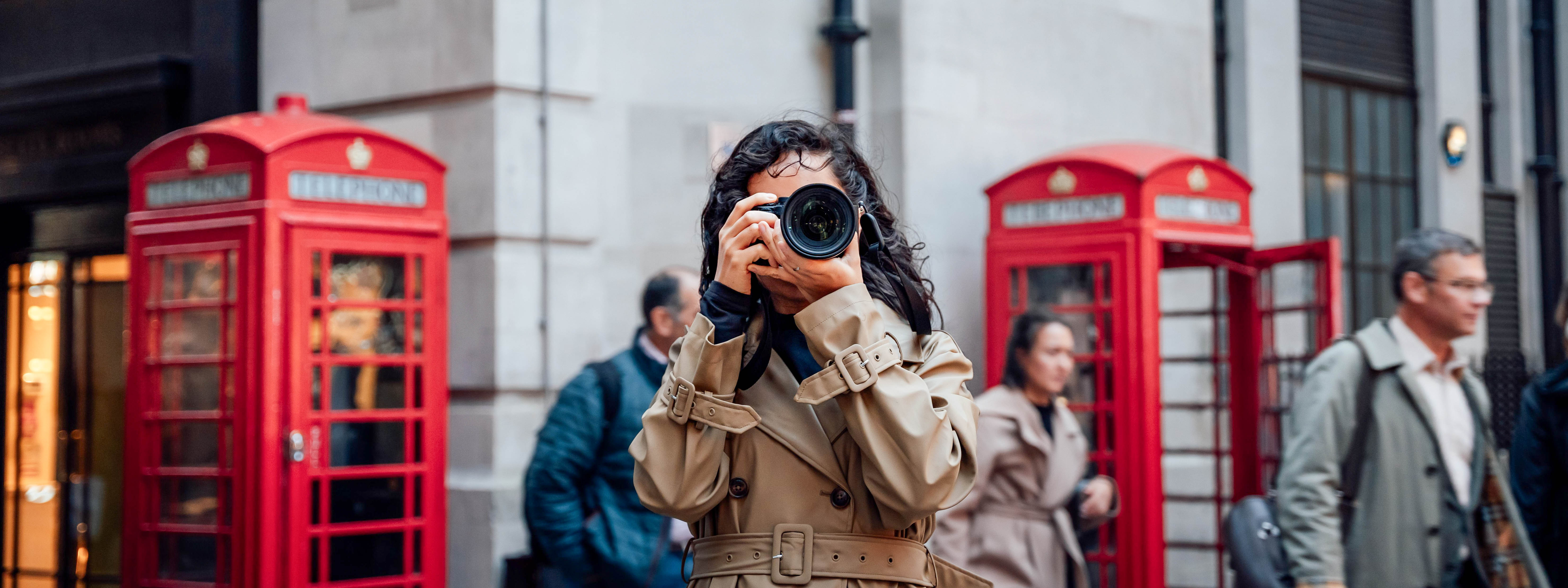 A woman with a camera in between two red London phone booths.