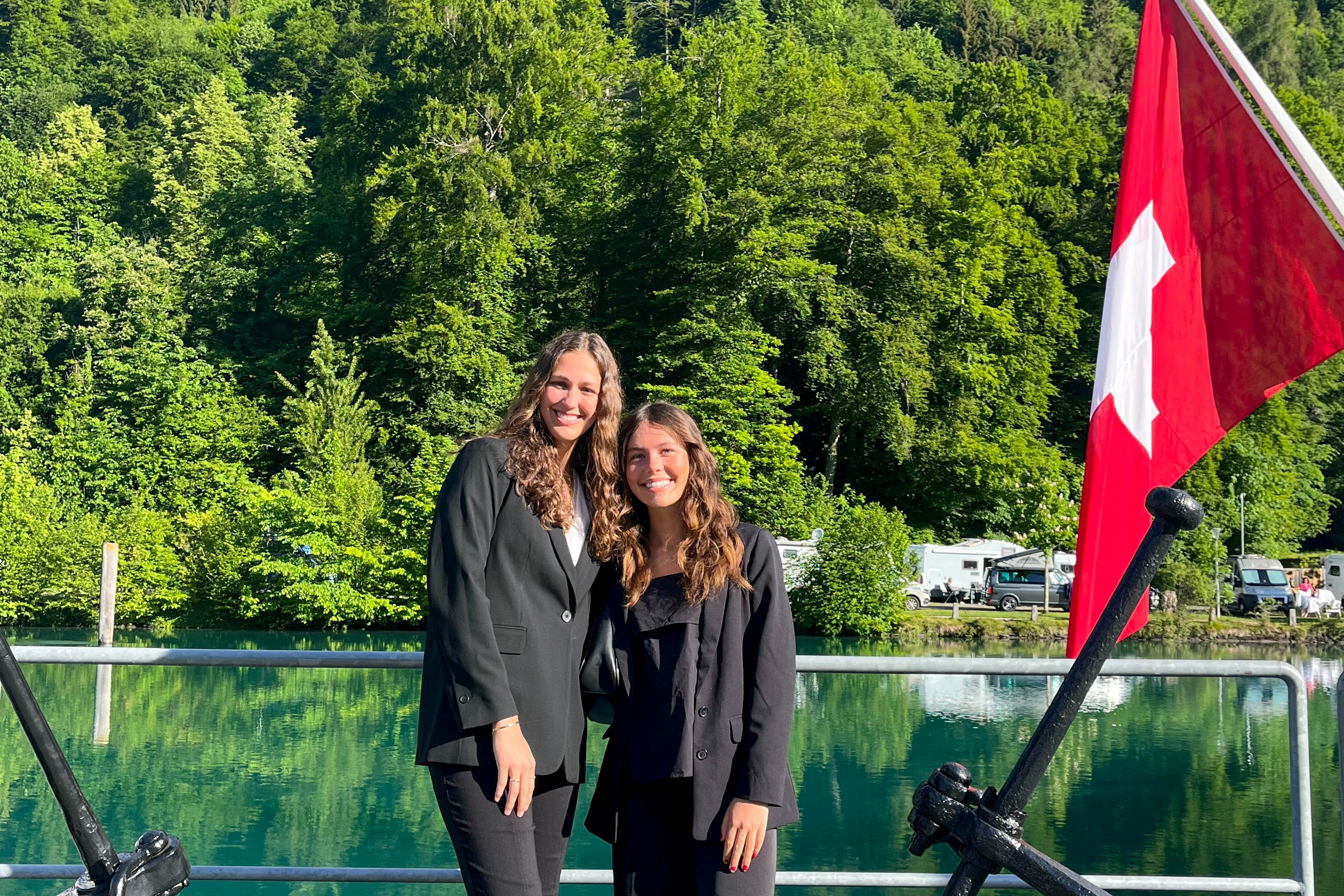 Students posing together in front of water and trees with a Swiss flag.
