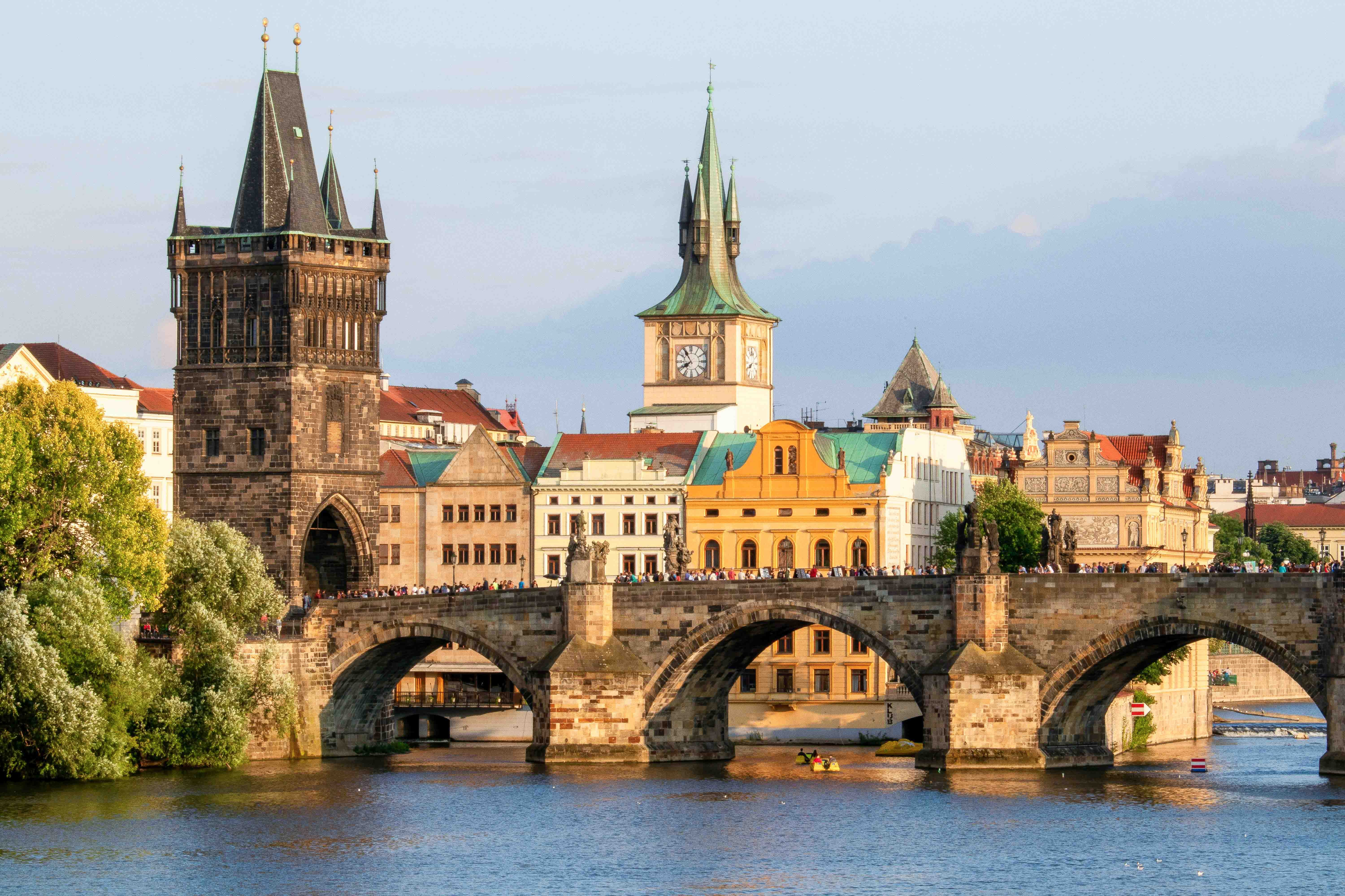 A view of historic buildings in Prague with a bridge and water in front of them.