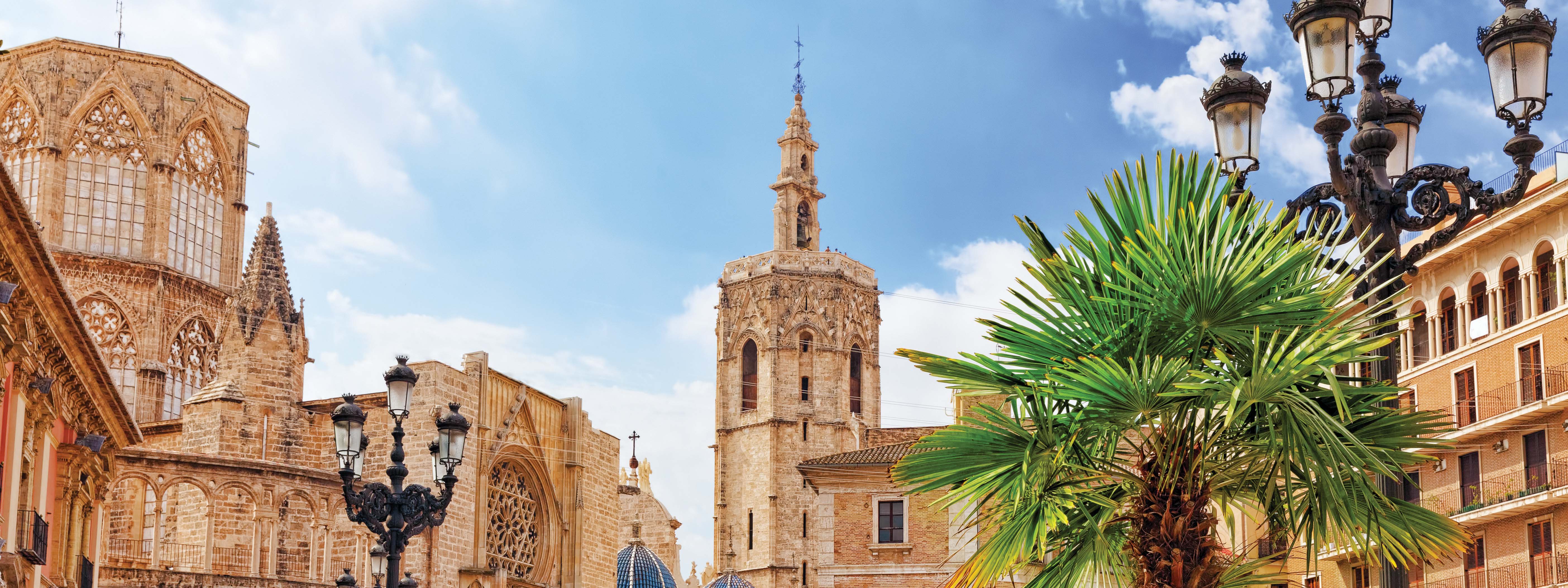 A view of Valencia's cathedral with lamp posts and palm trees in the foreground. 