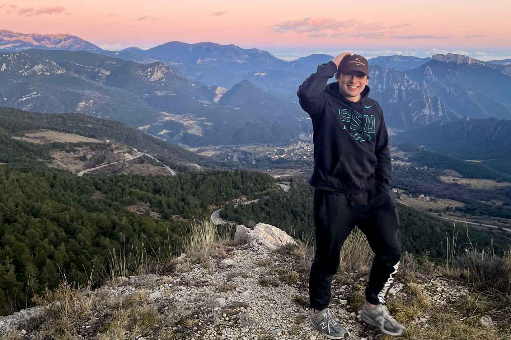 A student on a hike at sunset overlooking scenic mountains.