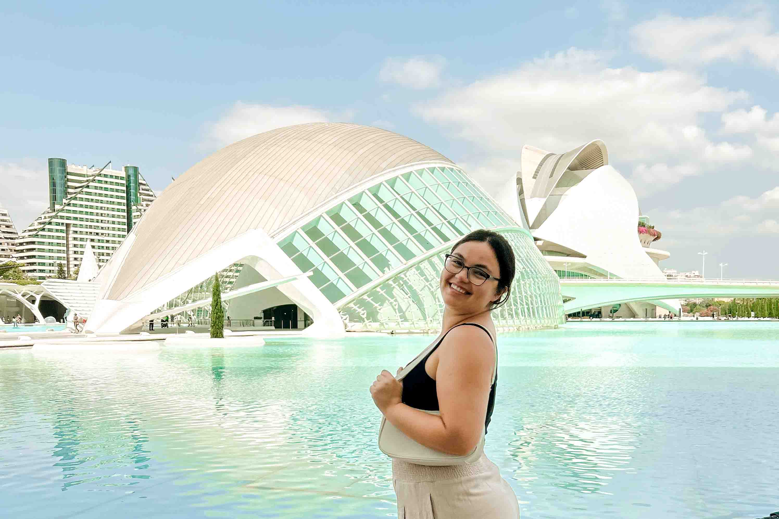 A poses in front of modern buildings and a pool at the City of Arts and Sciences in Valencia.