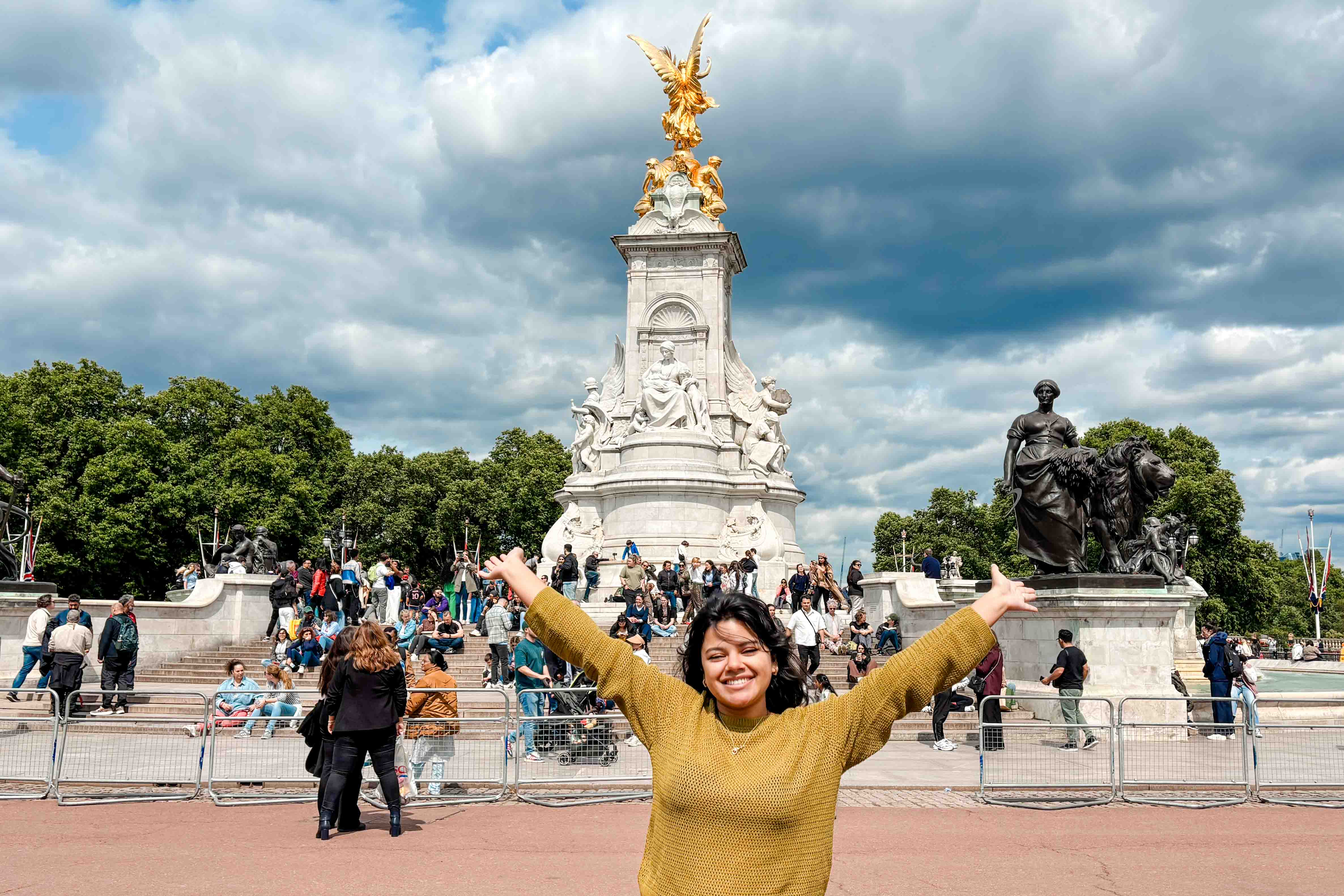 A student front of Buckingham Palace with her arms stretched above her head.