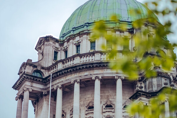 A view of a historic building in Belfast with foliage in front. 
