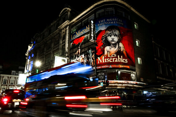Sign for Les Mis in London with a double decker bus driving by in a blur.