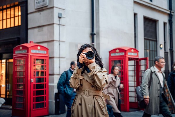 A woman holding a camera while standing between two red London phone booths.