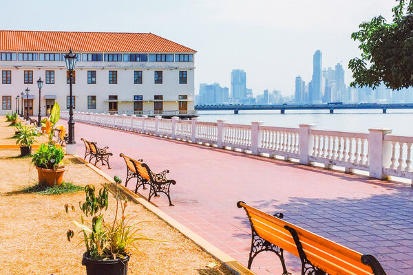 A view of Panama Viejo with a walkway and benches in the foreground and Panama City downtown in the distance.