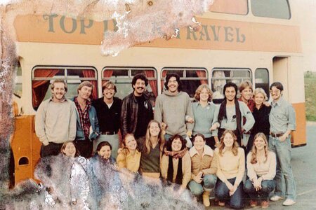 Students pose in front of a tour bus in an old worn photo.